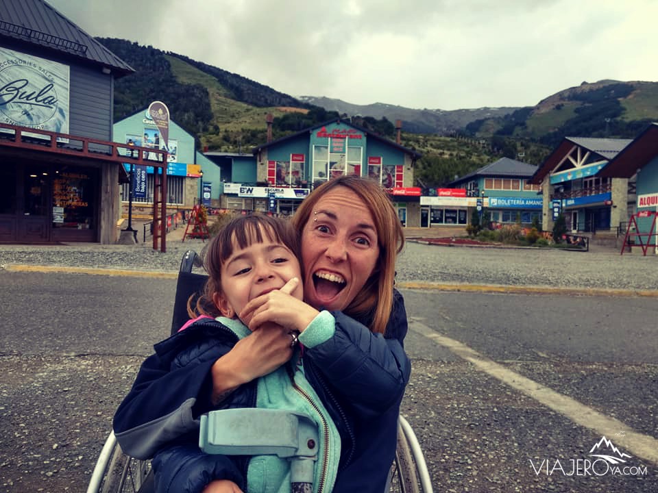 Naty sentada en la silla de ruedas y Sara mordiendo su dedo riendo con el Cerro Catedral de fondo Naty sentada en la silla de ruedas y Sara mordiendo su dedo riendo con el Cerro Catedral de fondo