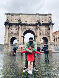 Edu y Sara abrazados con el coliseo romano de fondo en un día lluvioso